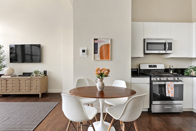 kitchen with dark wood-style flooring, baseboards, dark countertops, white cabinets, and appliances with stainless steel finishes