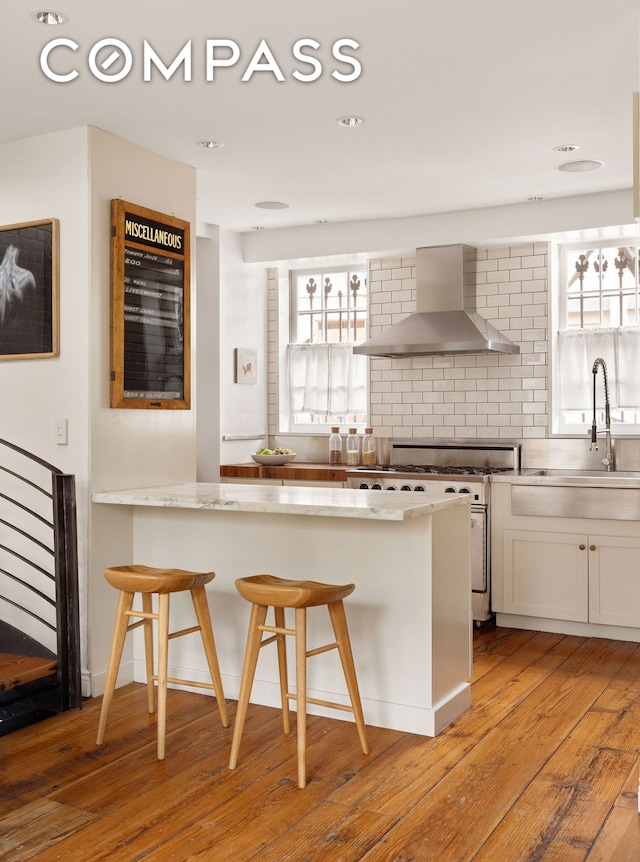 kitchen featuring wall chimney exhaust hood, white cabinets, a sink, light wood finished floors, and high end stainless steel range oven