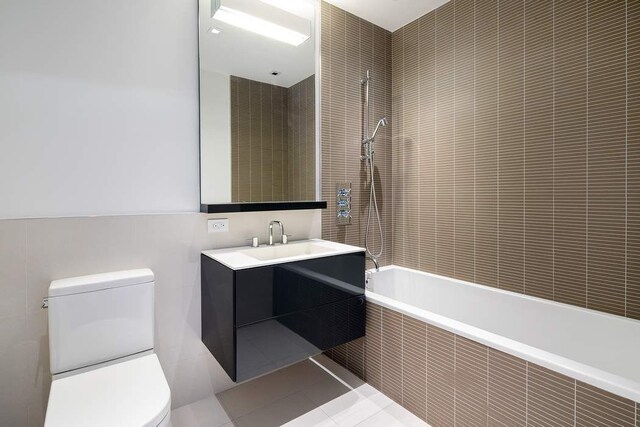 bathroom featuring tile patterned flooring, vanity, toilet, tiled shower / bath, and tile walls