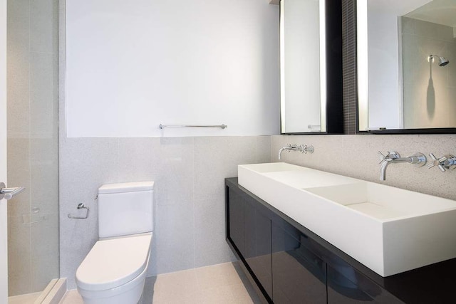 full bath with double vanity, toilet, tile walls, and a sink