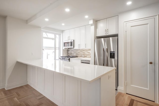kitchen featuring backsplash, a peninsula, light countertops, white cabinets, and appliances with stainless steel finishes