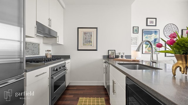 kitchen with dark wood finished floors, a sink, under cabinet range hood, stainless steel appliances, and white cabinetry