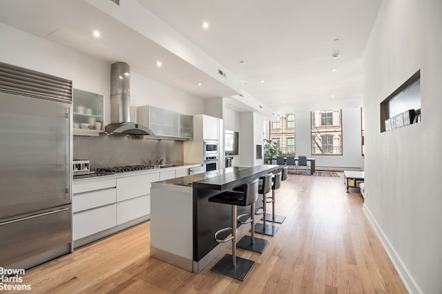 kitchen with exhaust hood, built in appliances, a breakfast bar area, a kitchen island, and modern cabinets