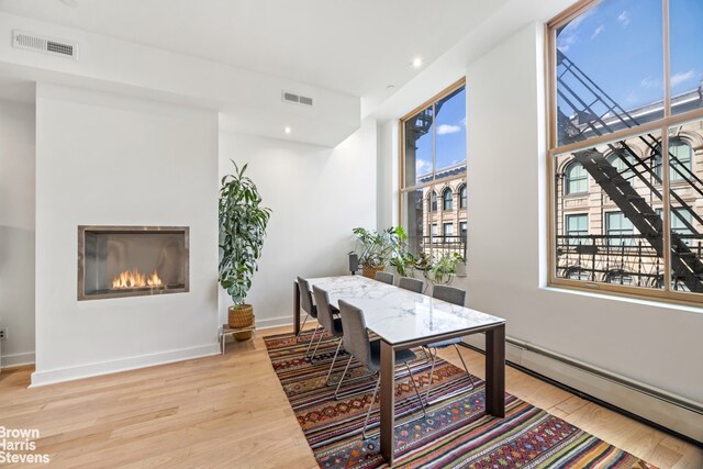 dining space featuring visible vents, a glass covered fireplace, baseboard heating, and light wood-type flooring