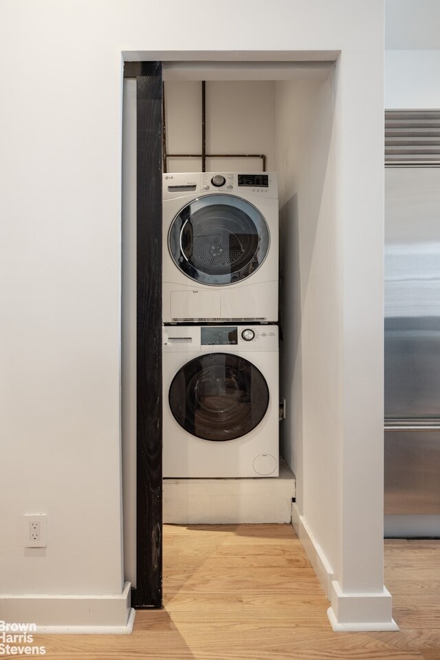 washroom featuring baseboards, stacked washer / drying machine, wood finished floors, and laundry area