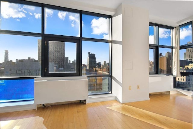 interior space featuring a city view, floor to ceiling windows, radiator heating unit, and hardwood / wood-style flooring