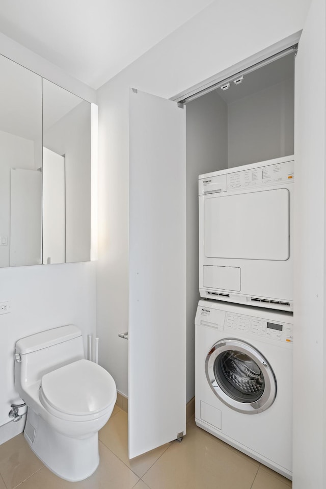 bathroom featuring toilet, tile patterned floors, stacked washing maching and dryer, and baseboards