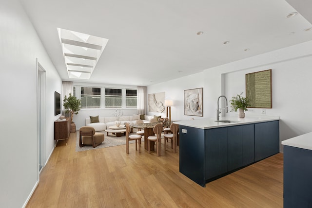 kitchen featuring a sink, light wood-style floors, light countertops, a skylight, and open floor plan