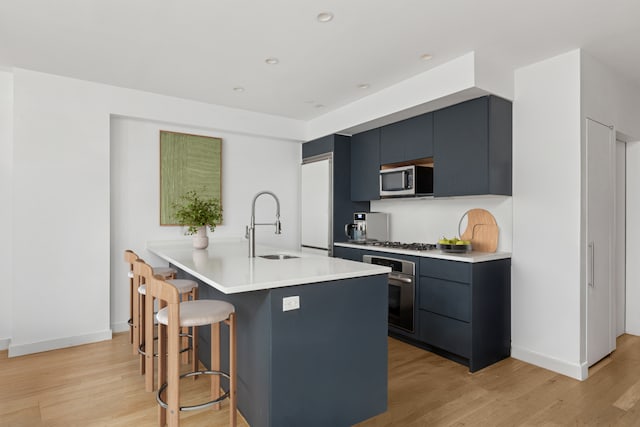 kitchen with a breakfast bar area, appliances with stainless steel finishes, light wood-style flooring, and a sink