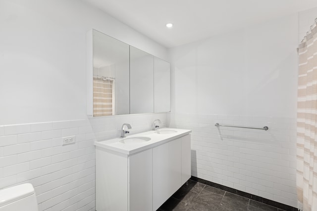 full bathroom with a sink, double vanity, a wainscoted wall, toilet, and tile walls