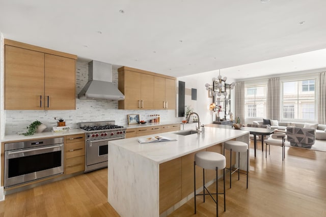 kitchen with a sink, wall chimney exhaust hood, light wood-style flooring, appliances with stainless steel finishes, and open floor plan