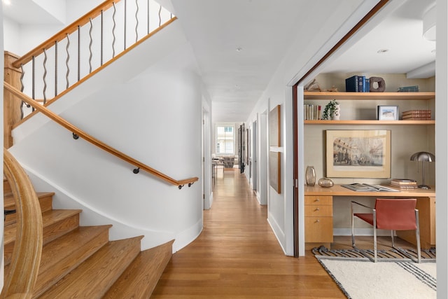 hall with light wood-style floors, baseboards, and stairs