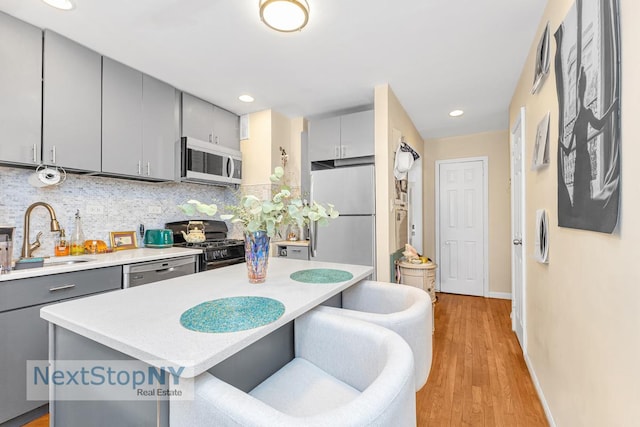 kitchen with a sink, stainless steel appliances, gray cabinets, backsplash, and baseboards
