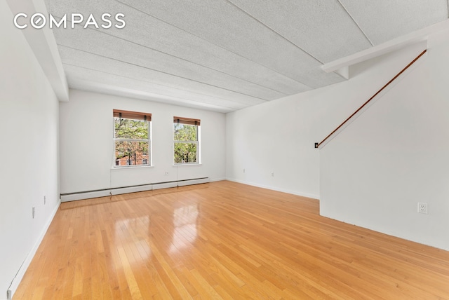 empty room with hardwood / wood-style flooring, a baseboard heating unit, and a textured ceiling