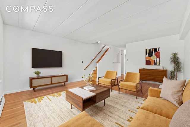 living area with stairs, wood finished floors, baseboards, and a baseboard radiator