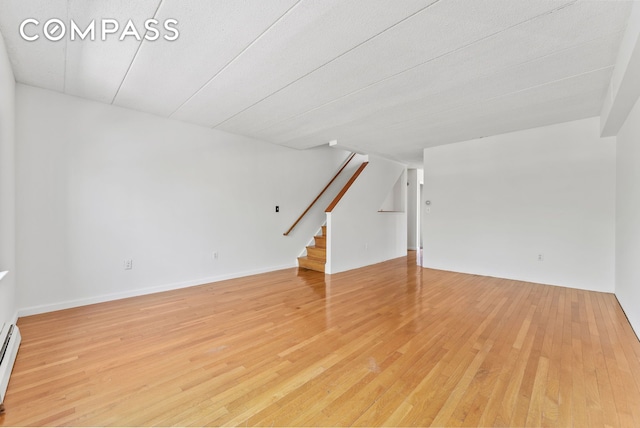 unfurnished room with stairway, light wood finished floors, and baseboard heating