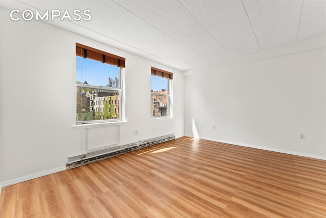 unfurnished room with baseboard heating, wood finished floors, and baseboards