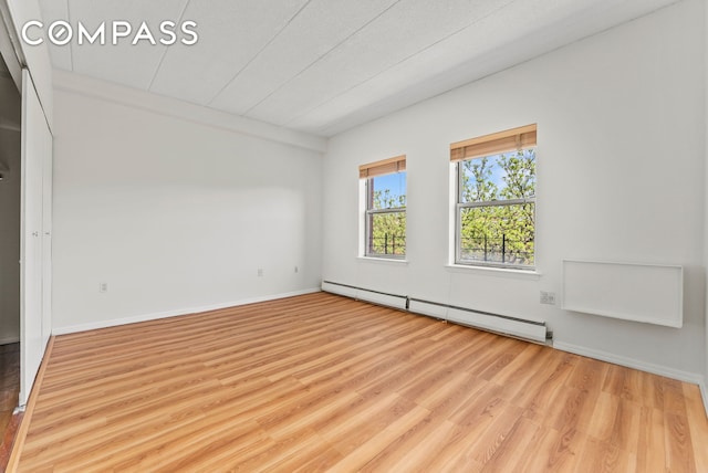 unfurnished room featuring a baseboard heating unit, wood finished floors, and baseboards