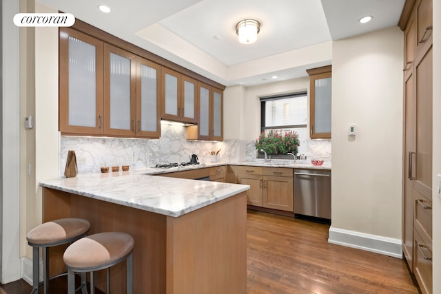 kitchen featuring a peninsula, a breakfast bar area, tasteful backsplash, light stone counters, and dishwasher
