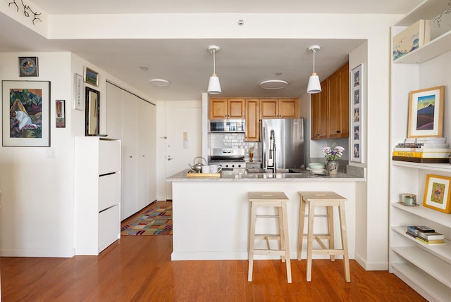425 Main St Unit 4-C, New York City, NY 10044 - kitchen with appliances with stainless steel finishes, wood finished floors, a peninsula, and backsplash
