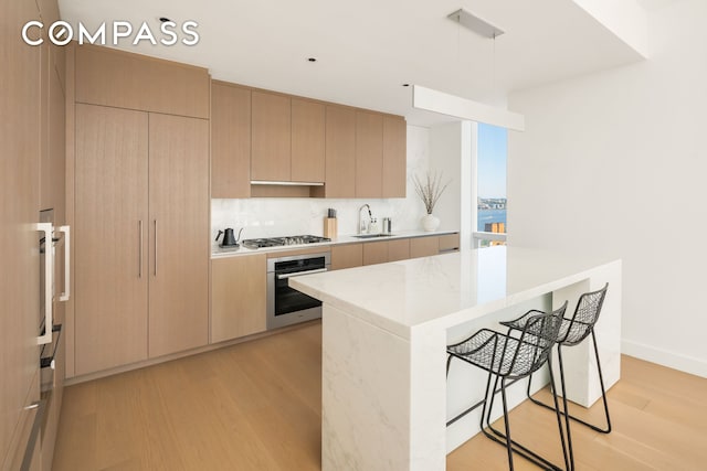 kitchen featuring a kitchen bar, modern cabinets, light countertops, light wood-style floors, and stainless steel appliances