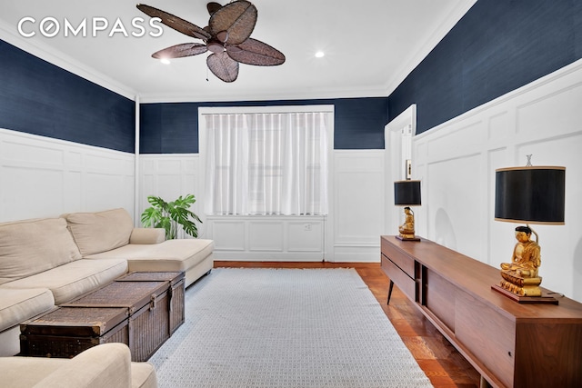 living area with a ceiling fan, ornamental molding, a wainscoted wall, and a decorative wall