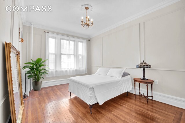bedroom with an inviting chandelier, ornamental molding, baseboards, and hardwood / wood-style flooring