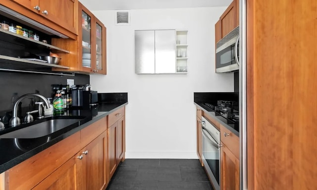 kitchen with glass insert cabinets, a sink, visible vents, stainless steel appliances, and brown cabinetry