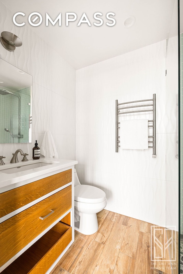 bathroom featuring vanity, toilet, radiator, wood finished floors, and a shower