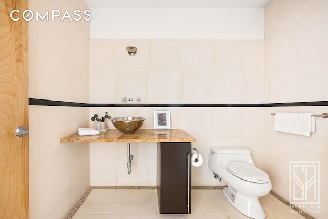bathroom featuring tile patterned flooring, a sink, toilet, and tile walls