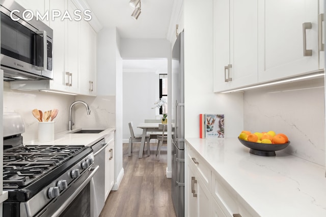 kitchen with wood finished floors, white cabinetry, light stone counters, a sink, and appliances with stainless steel finishes
