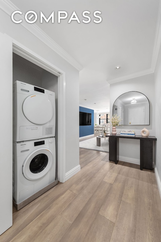 washroom featuring stacked washer / dryer, crown molding, arched walkways, baseboards, and light wood-style flooring