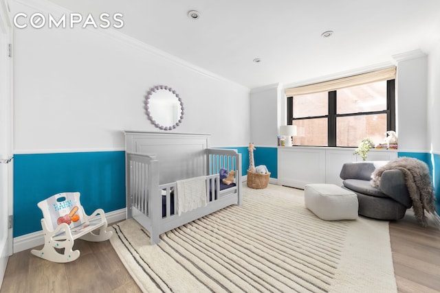 bedroom with baseboards, a crib, ornamental molding, and wood finished floors