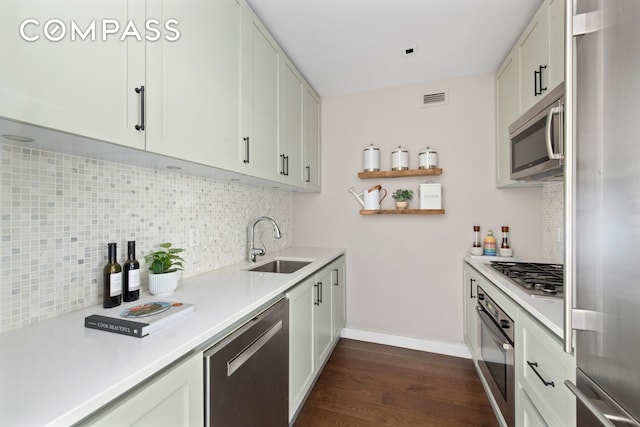 kitchen with appliances with stainless steel finishes, a sink, dark wood-type flooring, tasteful backsplash, and light countertops