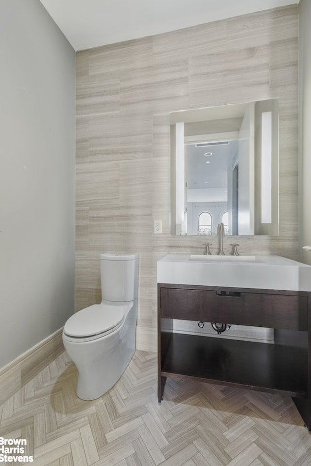 bathroom with vanity, baseboards, toilet, and tile walls