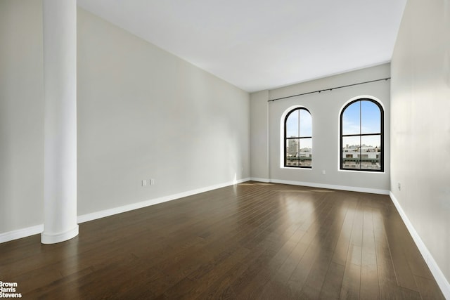 unfurnished room featuring baseboards and dark wood-style floors