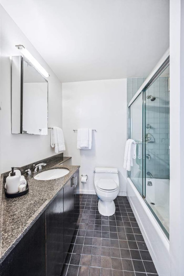 bathroom featuring tile patterned flooring, vanity, toilet, enclosed tub / shower combo, and baseboards