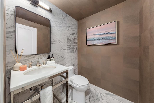 half bath with a sink, tile walls, toilet, and marble finish floor