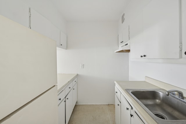 kitchen with a sink, freestanding refrigerator, under cabinet range hood, and white cabinetry