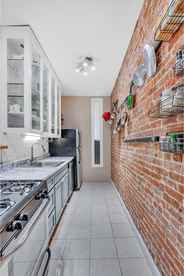 206 E 90th St Unit 4W, New York City, NY 10128 - kitchen featuring appliances with stainless steel finishes, a sink, brick wall, light tile patterned flooring, and glass insert cabinets