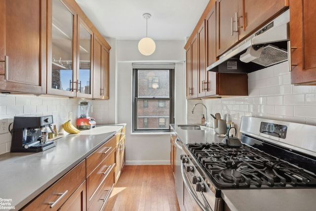 210 E Broadway Unit H1703, New York City, NY 10002 - kitchen with stainless steel gas range, a sink, under cabinet range hood, baseboards, and brown cabinets