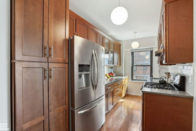 kitchen with light wood finished floors, brown cabinetry, stainless steel appliances, baseboards, and under cabinet range hood