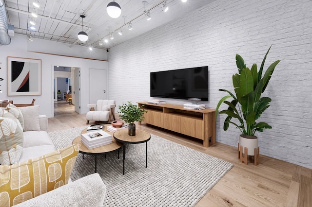 living area featuring a high ceiling, brick wall, rail lighting, and light wood finished floors