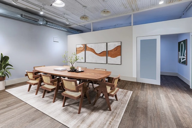 dining room featuring wood finished floors, baseboards, a high ceiling, and track lighting