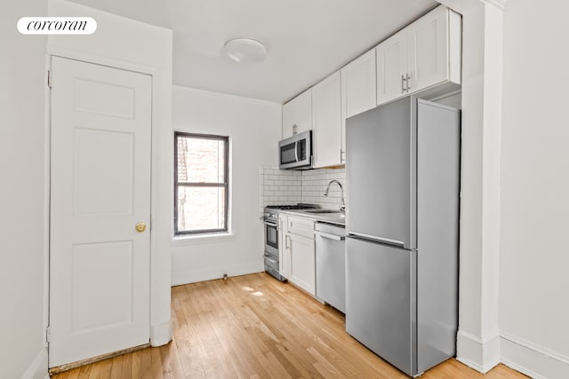 113 W 15th St Unit 1E, New York City, NY 10011 - kitchen with appliances with stainless steel finishes, white cabinetry, light wood-style floors, baseboards, and a sink