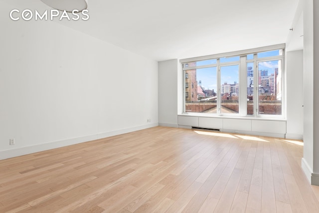 empty room with visible vents, a view of city, light wood-style flooring, and baseboards