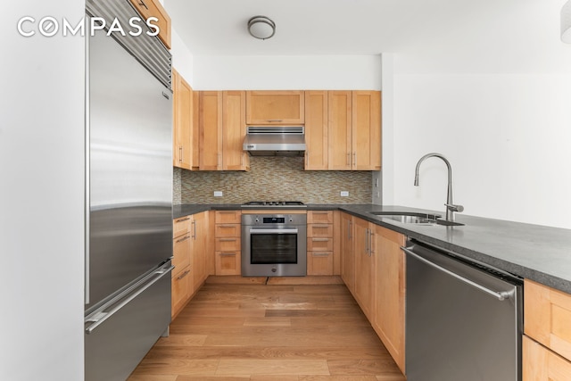 kitchen with a sink, appliances with stainless steel finishes, under cabinet range hood, and dark countertops