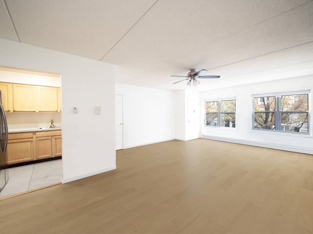 unfurnished living room with a ceiling fan, baseboards, a sink, and light wood-style floors