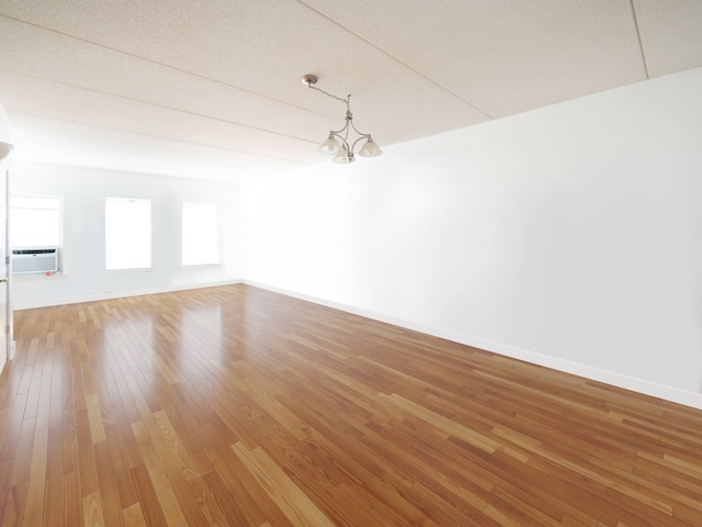 unfurnished room featuring baseboards, light wood finished floors, and an inviting chandelier