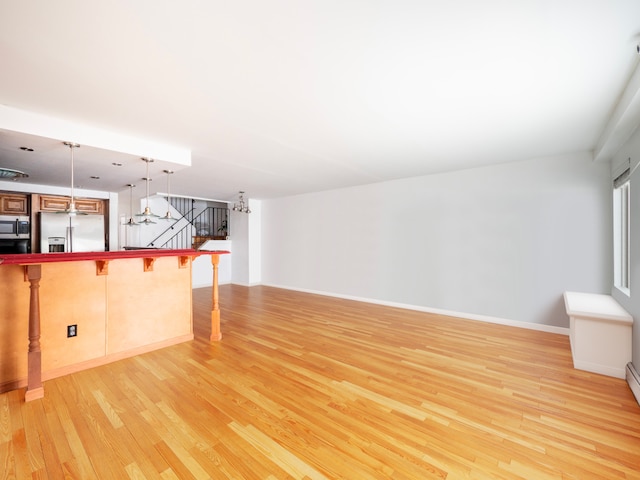 unfurnished living room featuring light wood-style floors, baseboards, and stairway